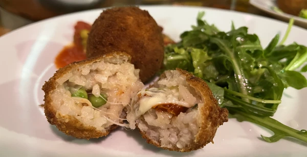 Zwei Arancini - im Vordergrund angeschnitten, im Hintergrund intakt - mit etwas Salat.